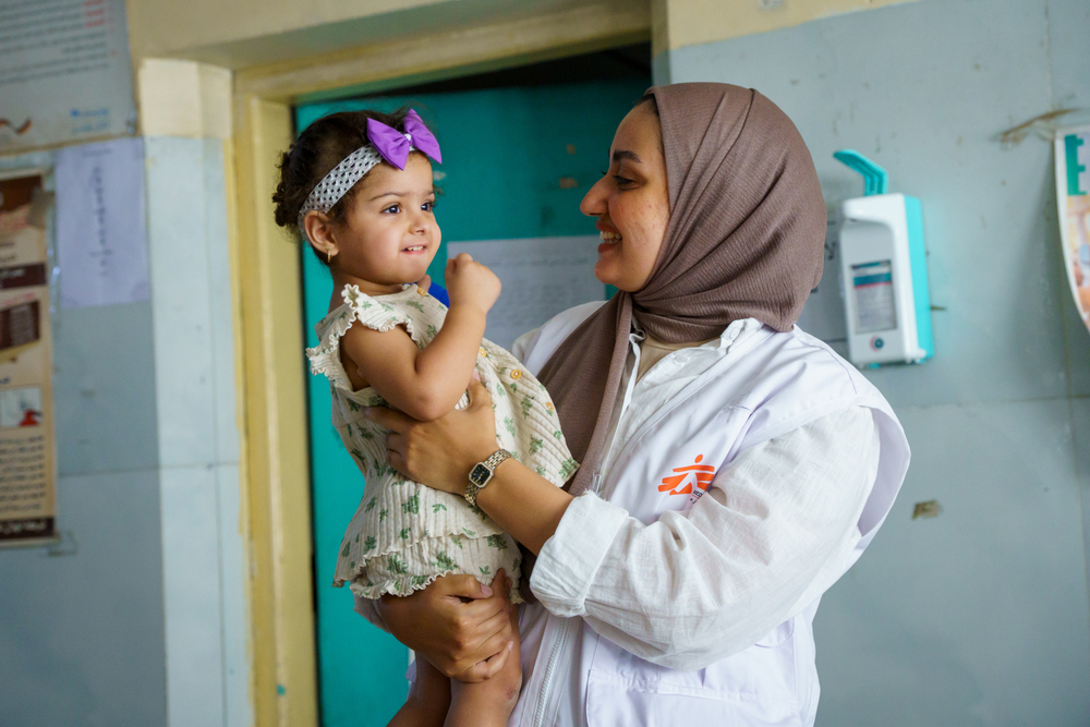 An MSF staff member holds a smiling young child at an MSF-supported clinic