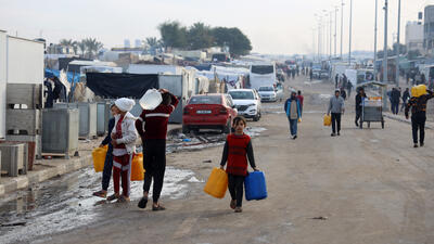 Palestinian men and children are carry water bottles in Tal Al-Sultan, a neighborhood in the
