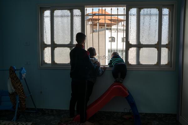 Hussam Odeh (L) and his cousins look from their window towards an Israeli soldier in Huwara on 13 April 2023. 