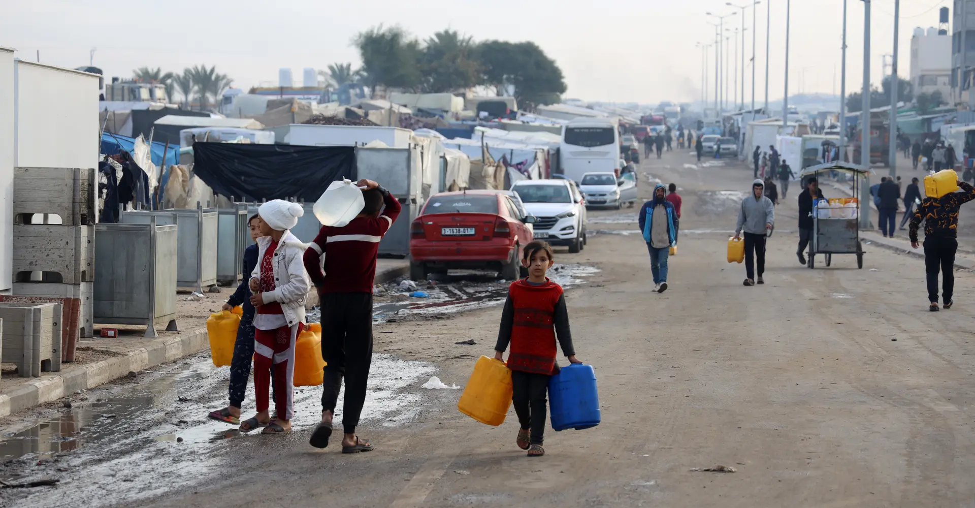 Palestinian men and children are carry water bottles in Tal Al-Sultan, a neighborhood in the