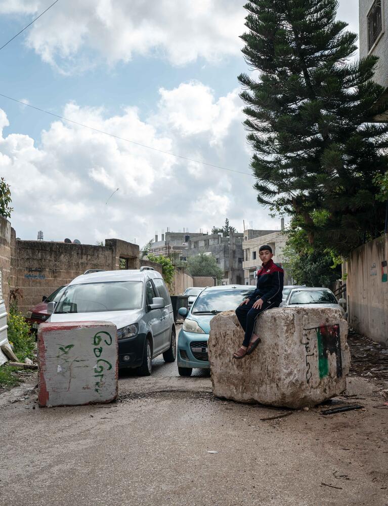 Hussam Odeh sits on a roadblock placed by Israeli soldiers in his neighborhood outside his home in Huwwara on 13 April 2023